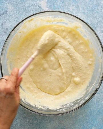 two hands mixing tres leches cake batter in a glass bowl.