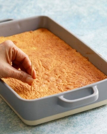 a hand poking holes in a baked tres leches cake using a tooth pick.