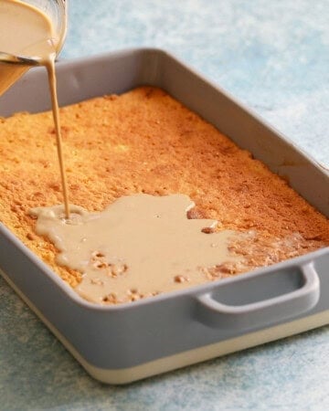 a hand pouring brown milk into a baked cake in a rectangular cake pan.
