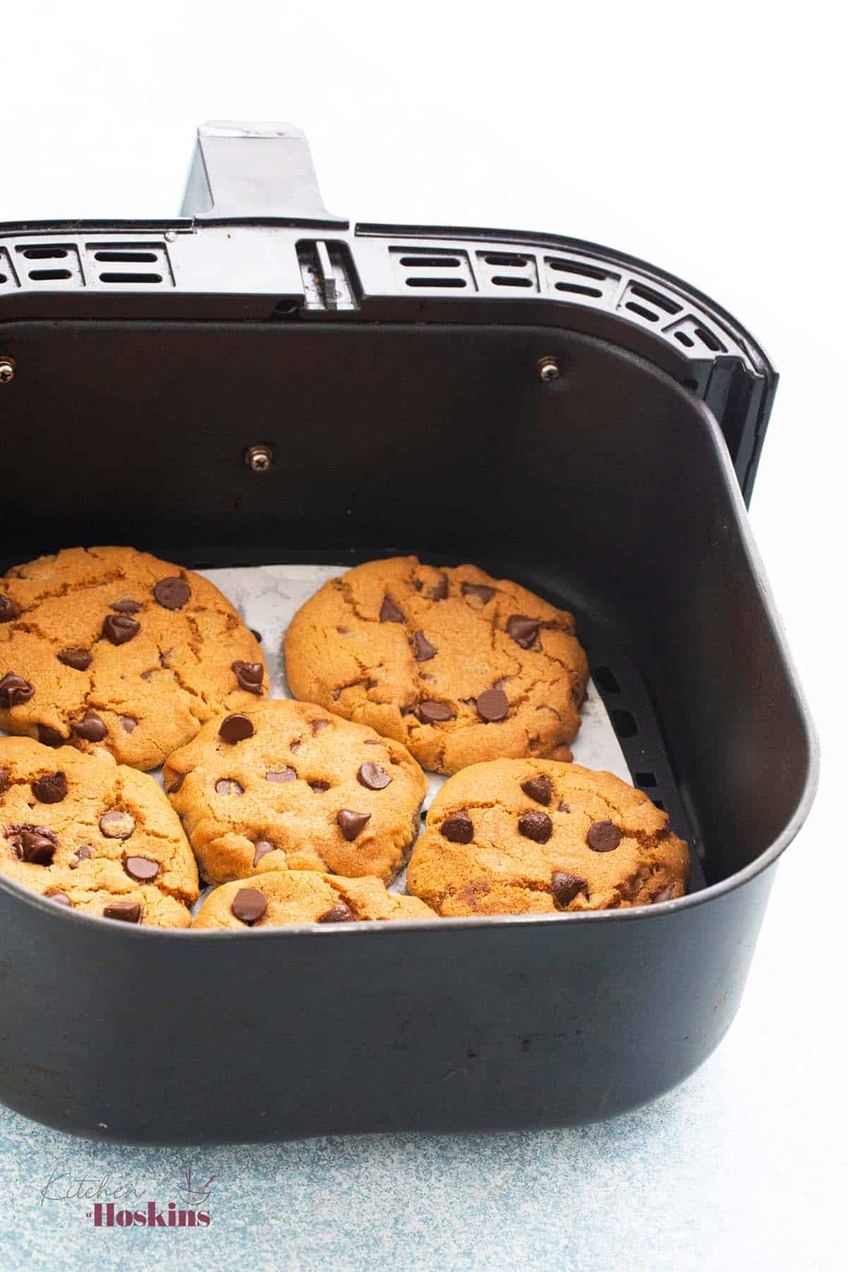 a air fryer basket with 6 chocolate chip cookies.