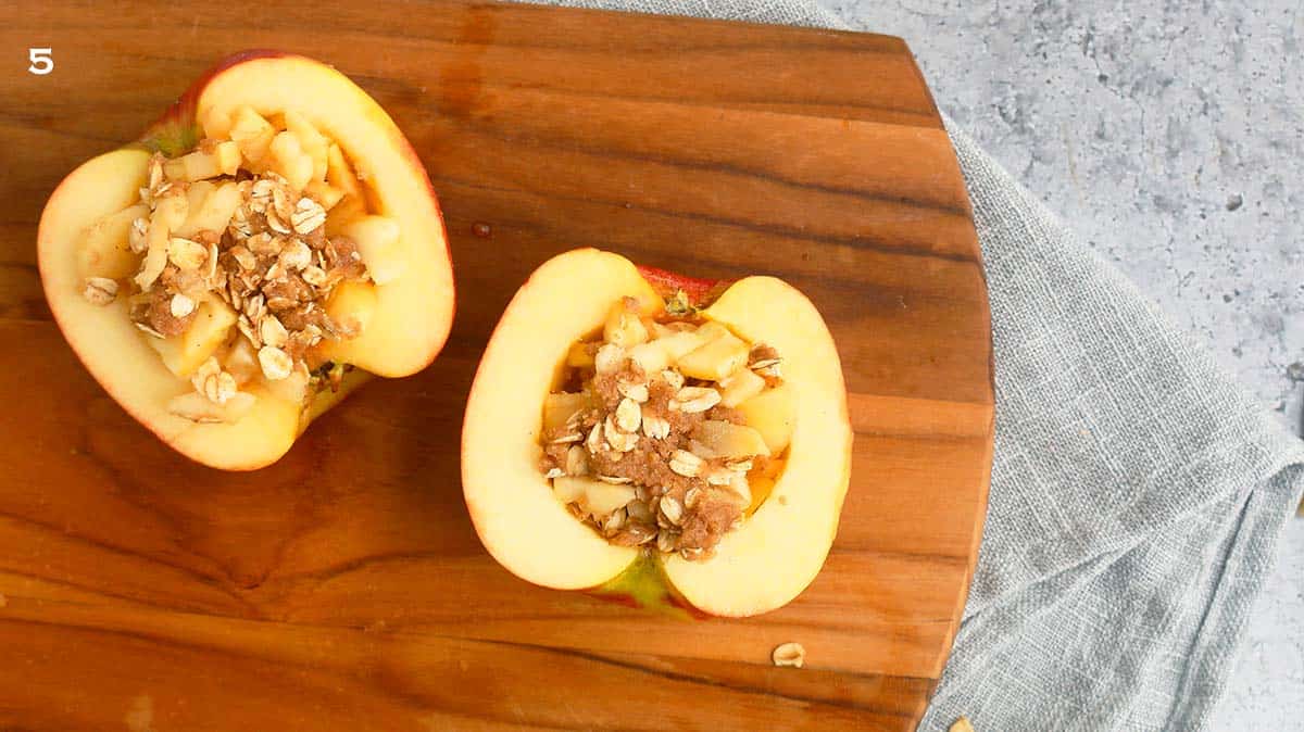 2 apple halves filled with stuffing on a wooden board.