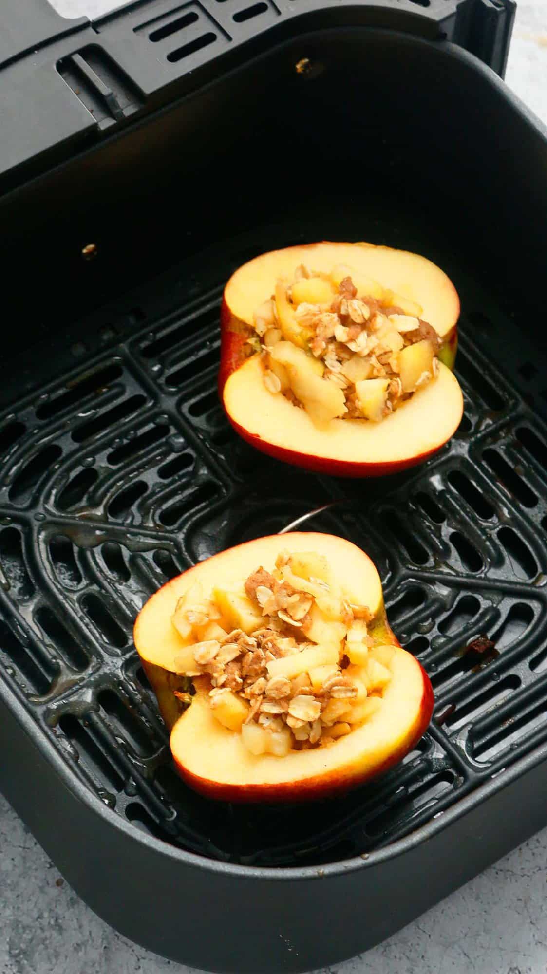 2 stuffed apple halves in a air fryer basket.