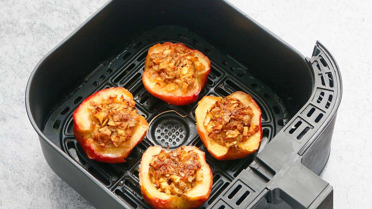 4 baked apple halves in an air fryer basket.