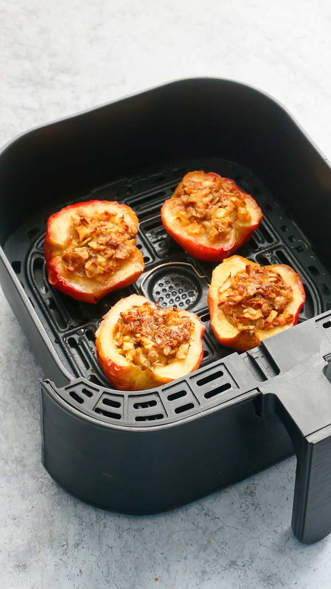 4 baked apple halves in an air fryer basket.