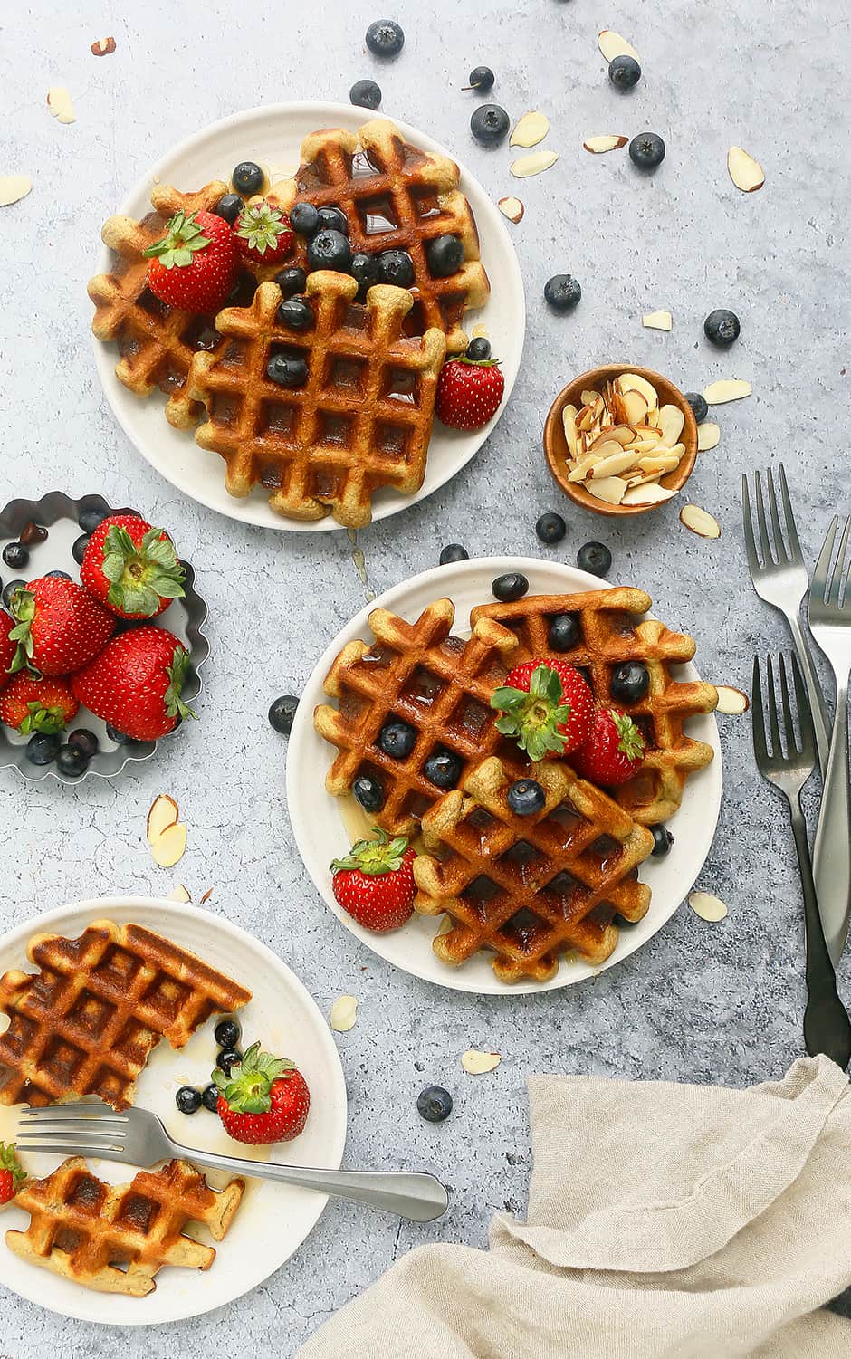 white plates with healthy homemade waffles, garnished with fresh berries and sliced almonds and stainless steel forks for eating