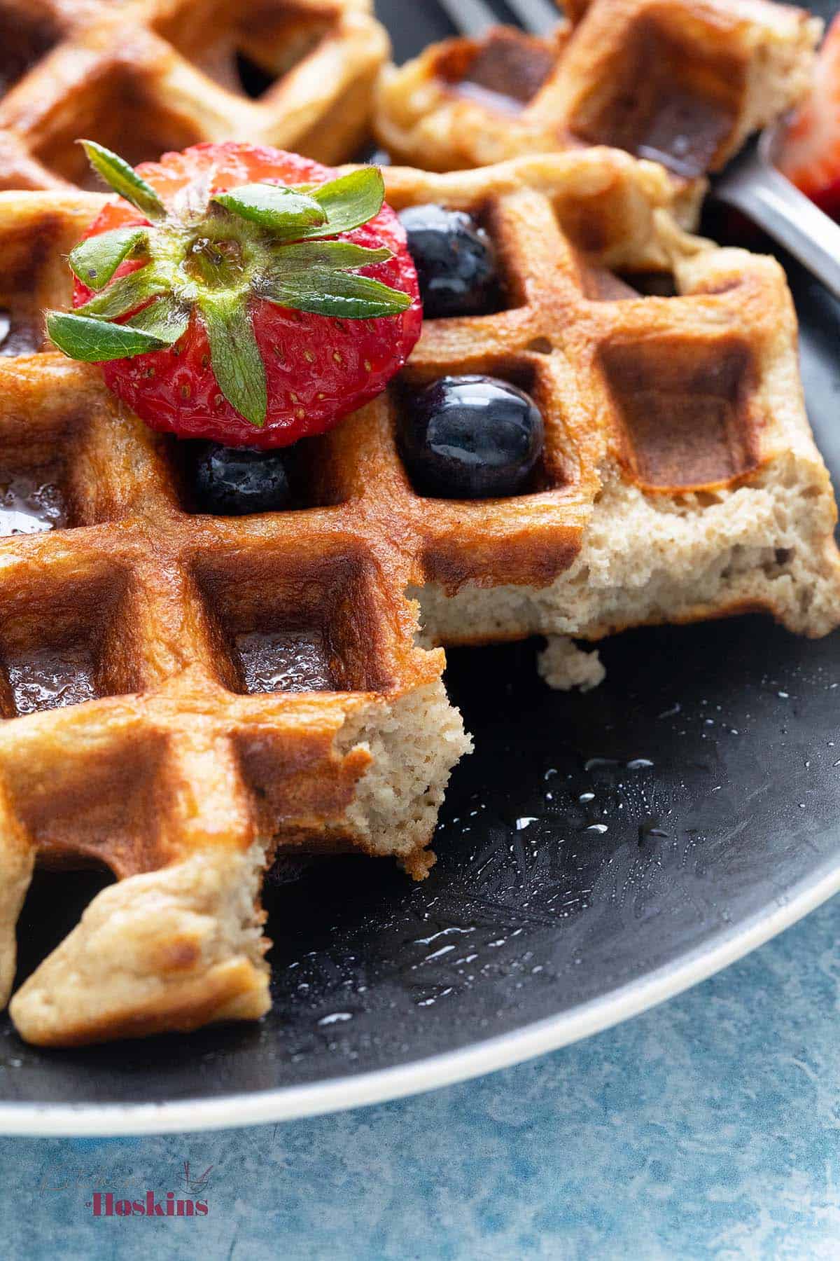 a broken waffle in a black plate topped with berries.