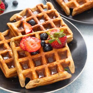 3 waffles on a black plate topped with berries.