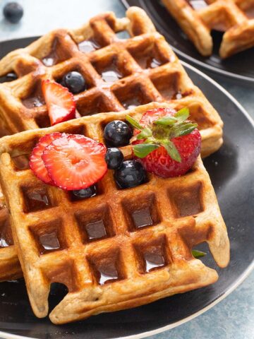 3 waffles on a black plate topped with berries.