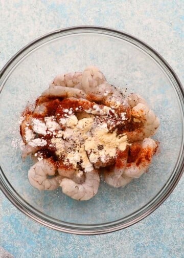 raw shrimp topped with spices in a glass bowl.