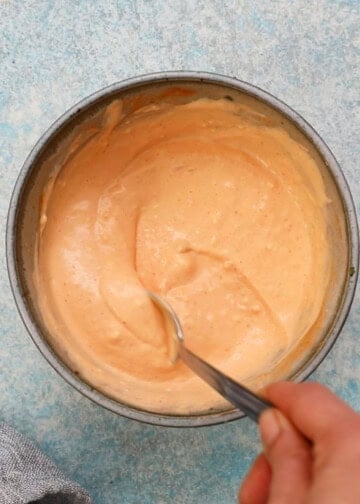 a hand mixing pink sauce in a grey bowl using a metal spoon.