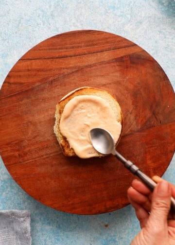 a hand spreading pink sauce on a toasted bun.