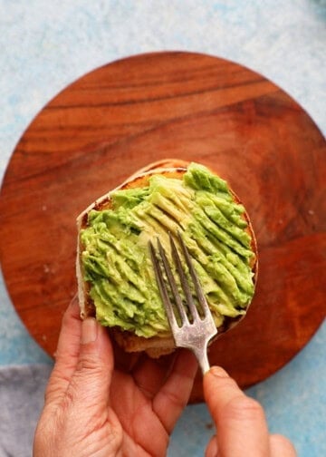 a hand mashing green avocado on a bun.