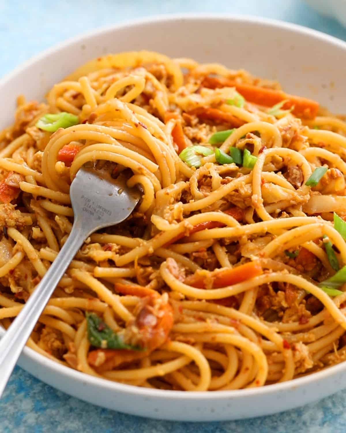 spicy thai noodles in a white bowl along with a fork.