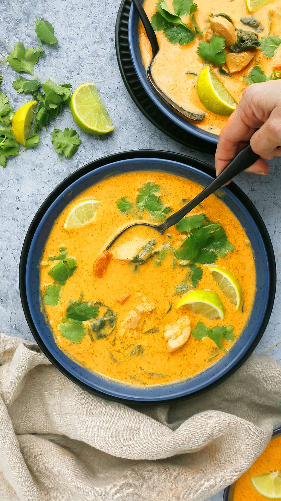 a blue bowl with red thai soup garnished with lime wedges and cilantro