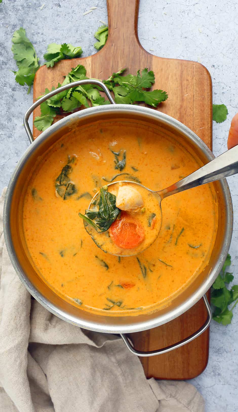 a stainless steel sauce pan with thai red curry chicken soup placed on a wooden board and garnished with cilantro