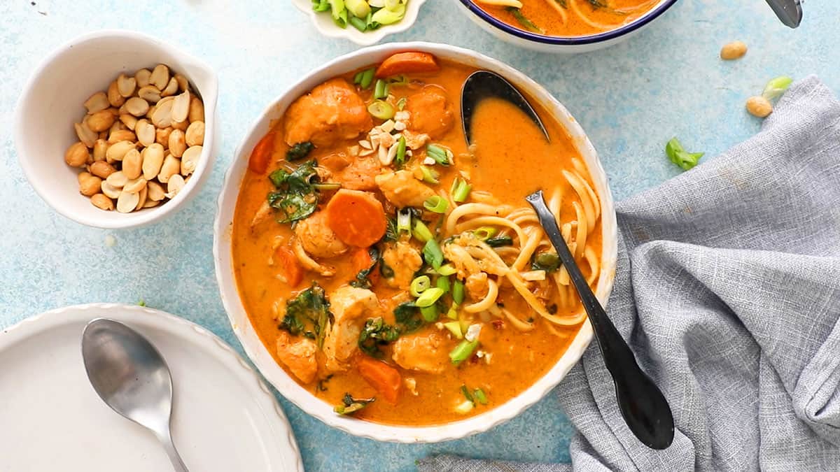 orange thai chicken soup with yellow noodles in a white bowl.