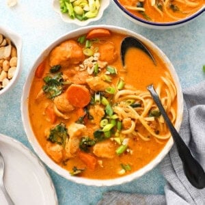 orange thai chicken soup with yellow noodles in a white bowl.