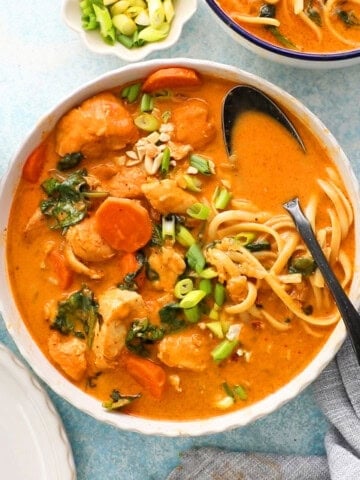 orange thai chicken soup with yellow noodles in a white bowl.