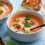 pink colored tomato soup topped with green basil in a white bowl.