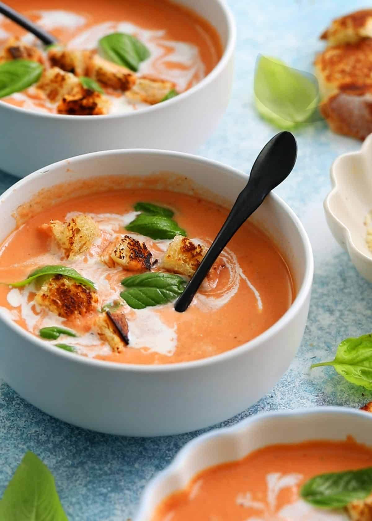 pink colored tomato soup topped with green basil in a white bowl.