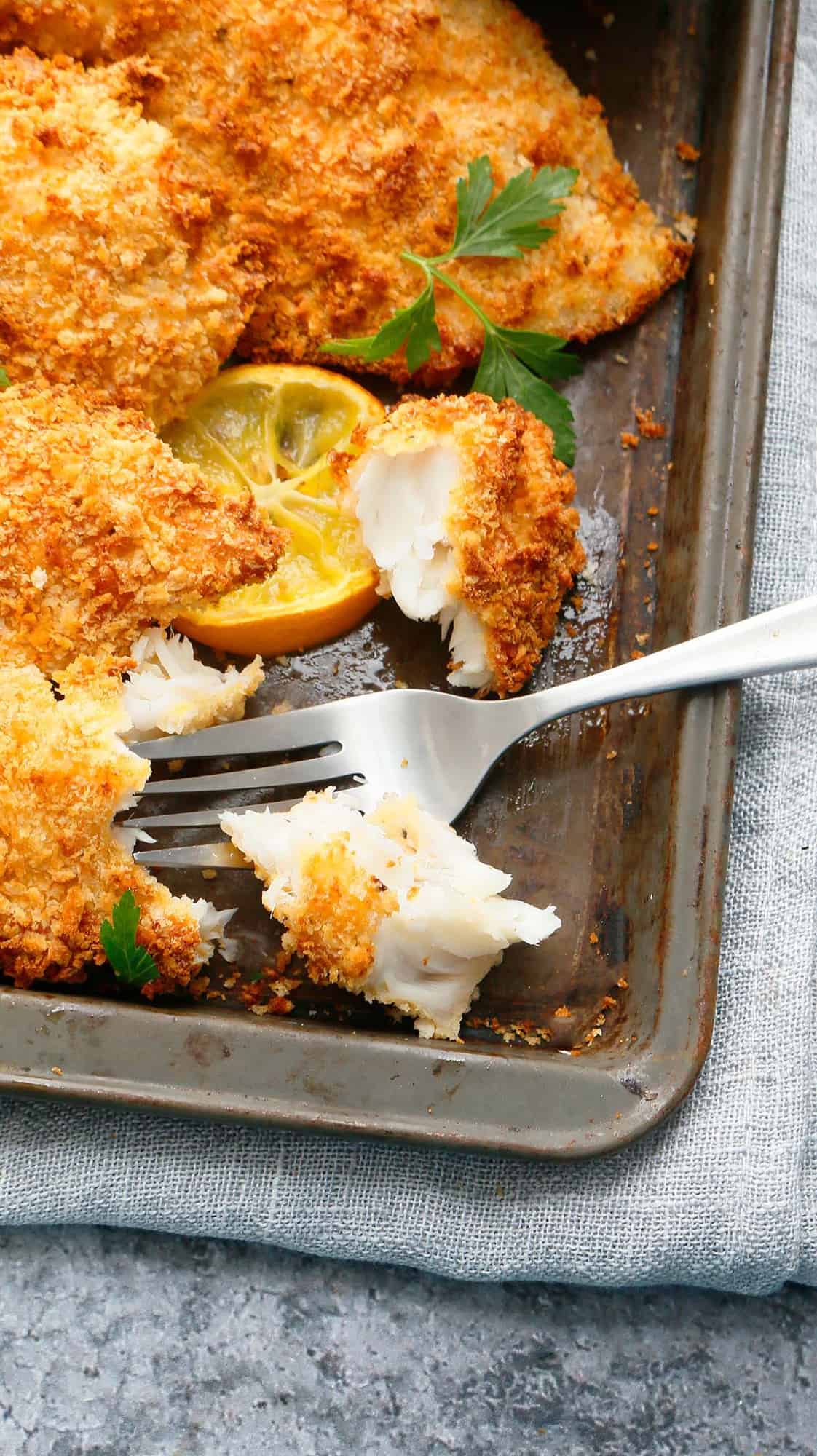 panko crusted fish fillets on a baking sheet with fork.