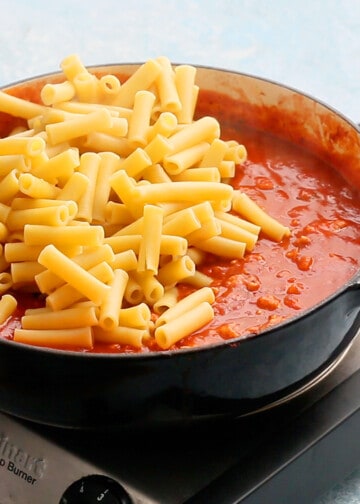 cooked ziti pasta on top of red marinara sauce in a large white skillet.