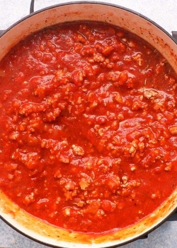 red marinara sauce mixed with cooked chicken meat in a large white skillet.