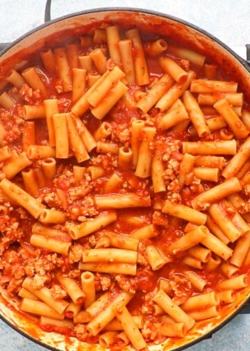cooked ziti pasta tossed in red marinara sauce in a large white skillet.