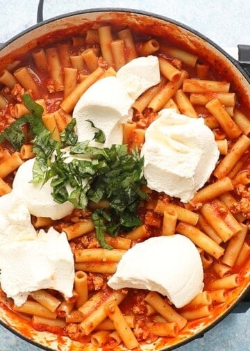 scoops of ricotta cheese and chopped fresh basil leaves placed on top of ziti pasta in a large pan.