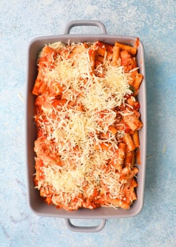 cooked red ziti pasta topped iwth shredded white cheese in a rectangular grey baking dish. 