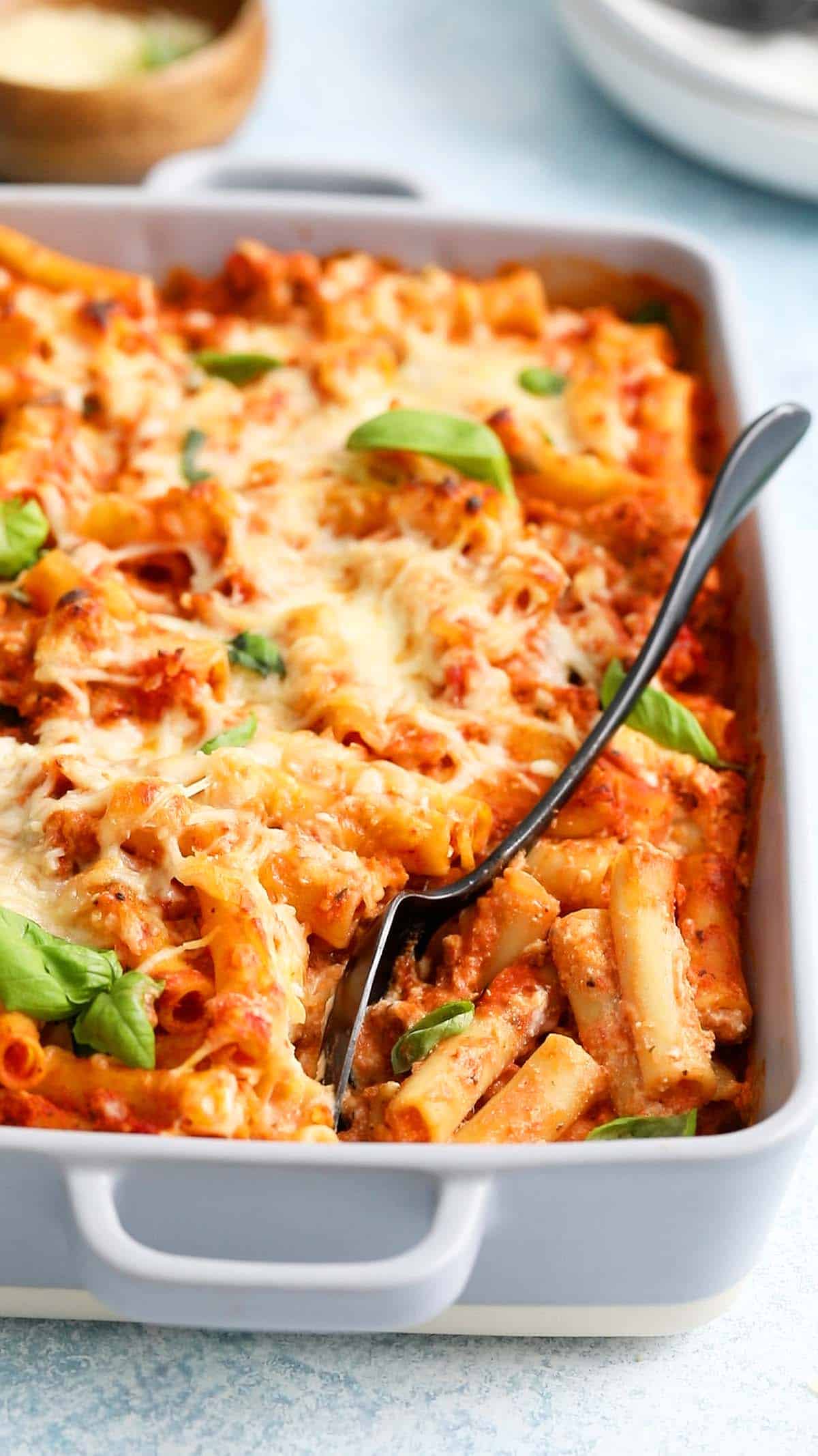 baked ziti pasta in a grey casserole dish along with a black spoon.