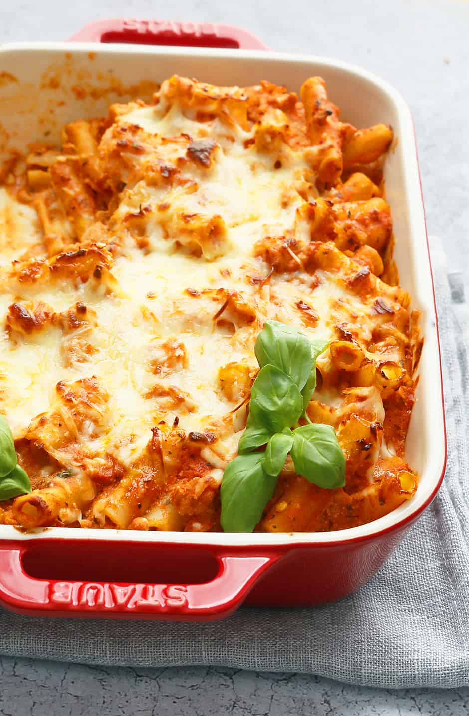 red handled casserole dish with ground chicken baked ziti and garnished with fresh basil