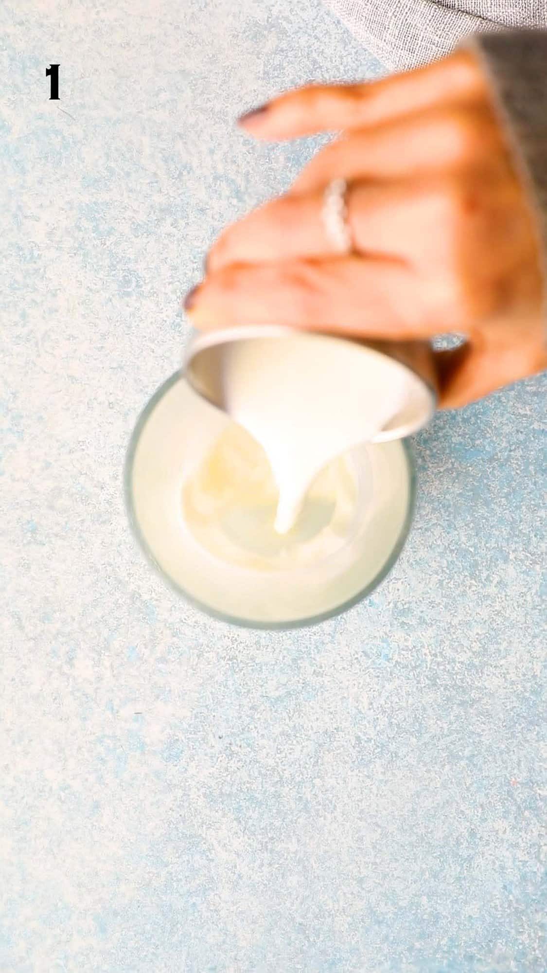 a hand pouring milk into a glass mug.