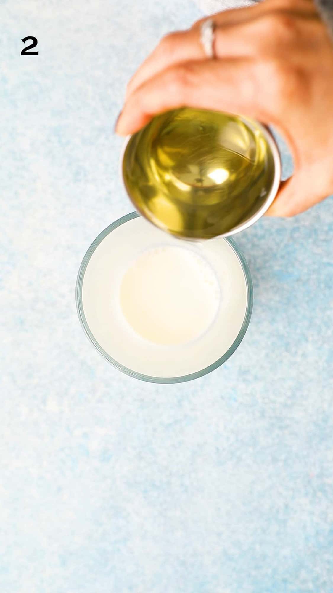 a hand pouring oil into a glass mug.