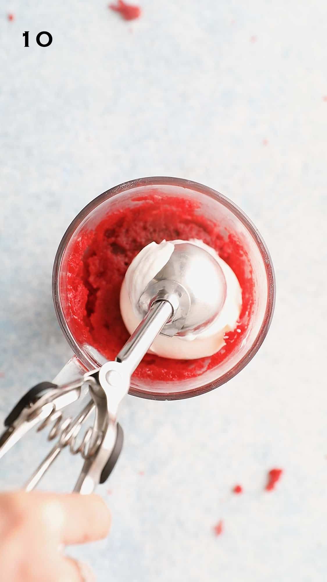 a hand topping yogurt with an ice cream scoop on a mug cake.