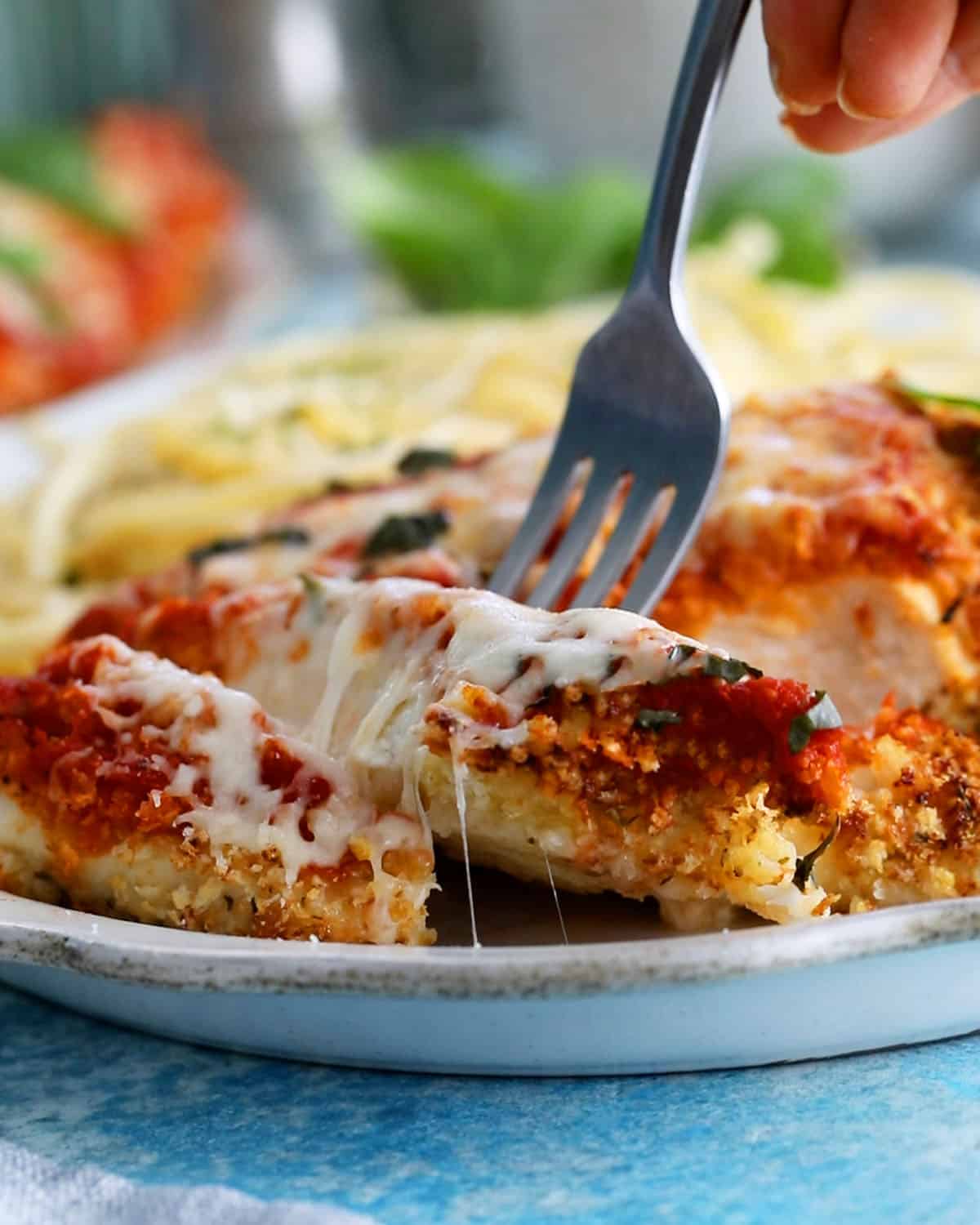 red and white chicken parmesan with yellow pasta in a white plate.