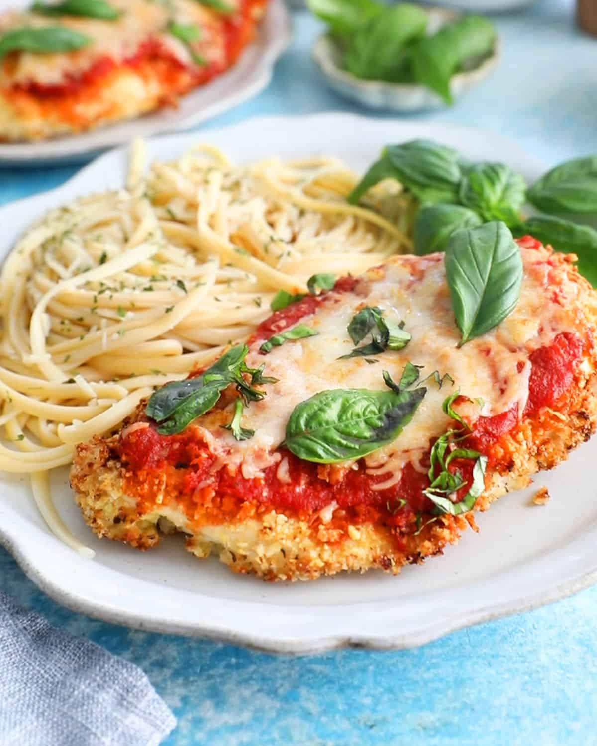red and white chicken parmesan with yellow pasta in a white plate.