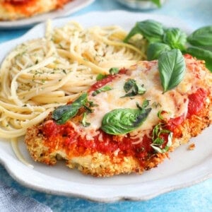 red and white chicken parmesan with yellow pasta in a white plate.