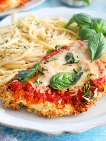 red and white chicken parmesan with yellow pasta in a white plate.