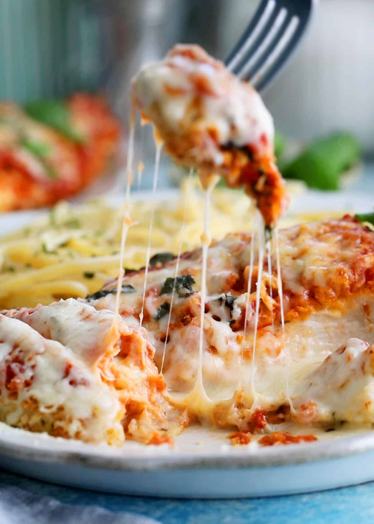 red and white chicken parmesan with yellow pasta in a white plate.