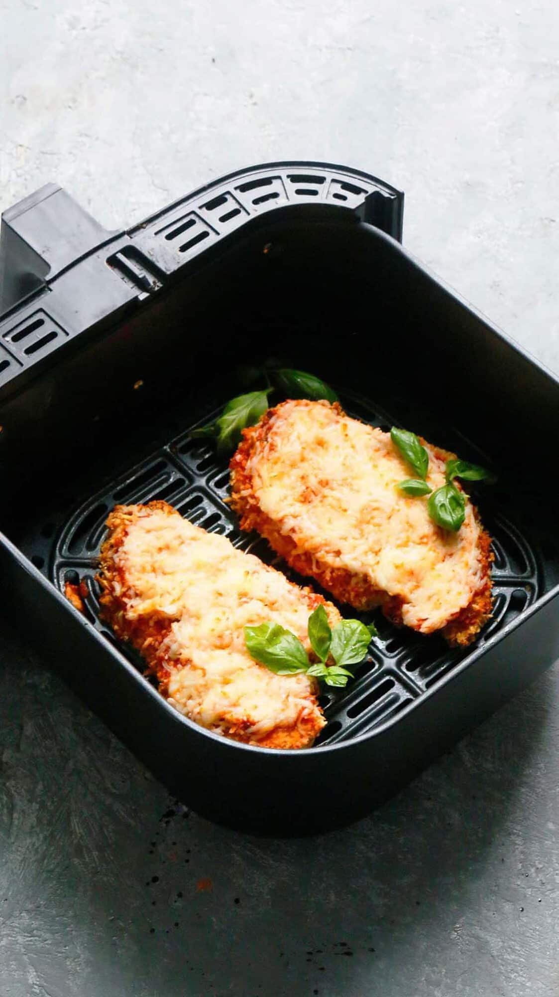 2 cooked chicken parmesan cutlets in a air fryer basket.