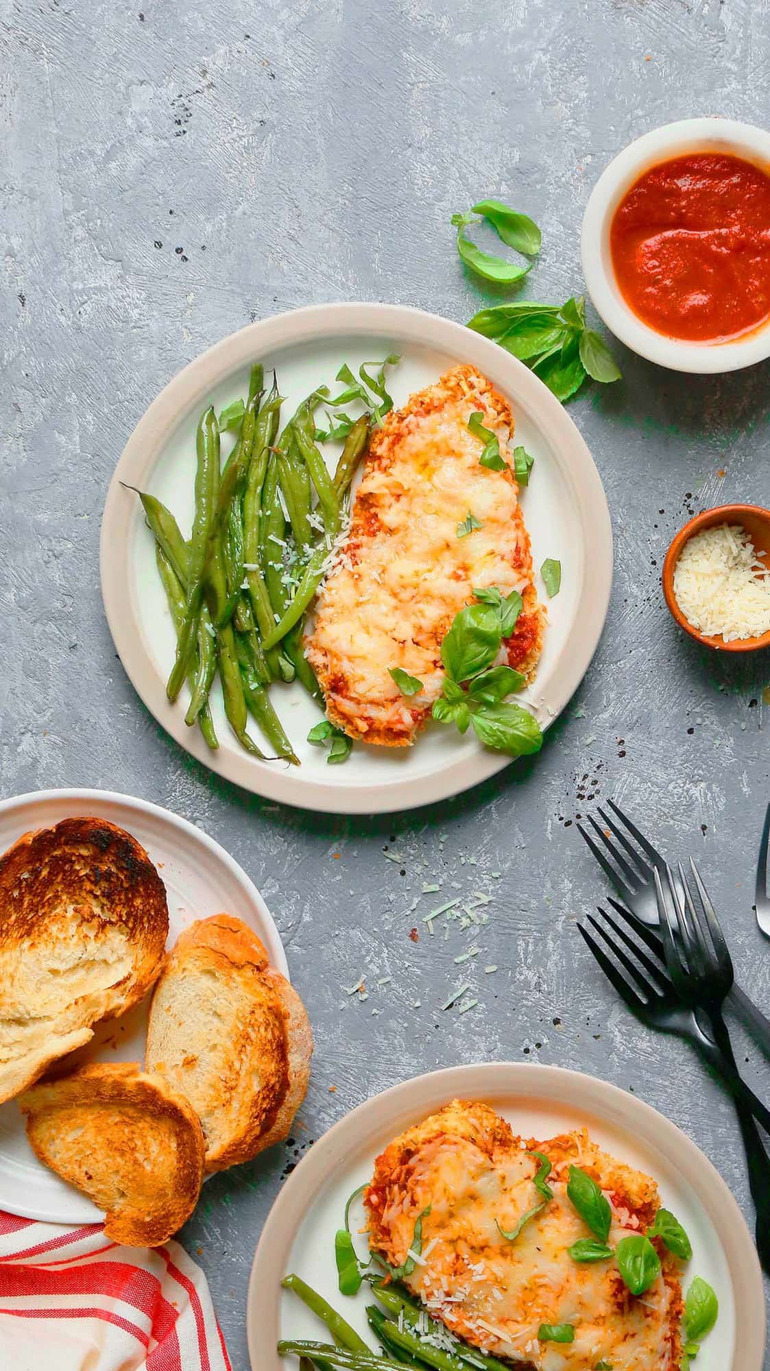 white dinner plates with chicken parmigiana served along with roasted green beans