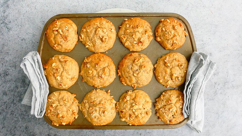 a muffin pan with freshly baked eggless banana muffins with grey towels on either side