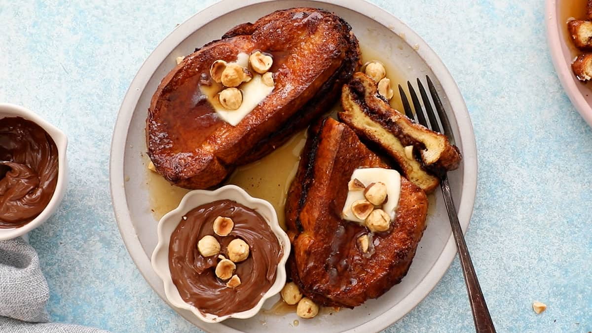 two brown French toasts topped with butter and hazelnuts in a white plate.