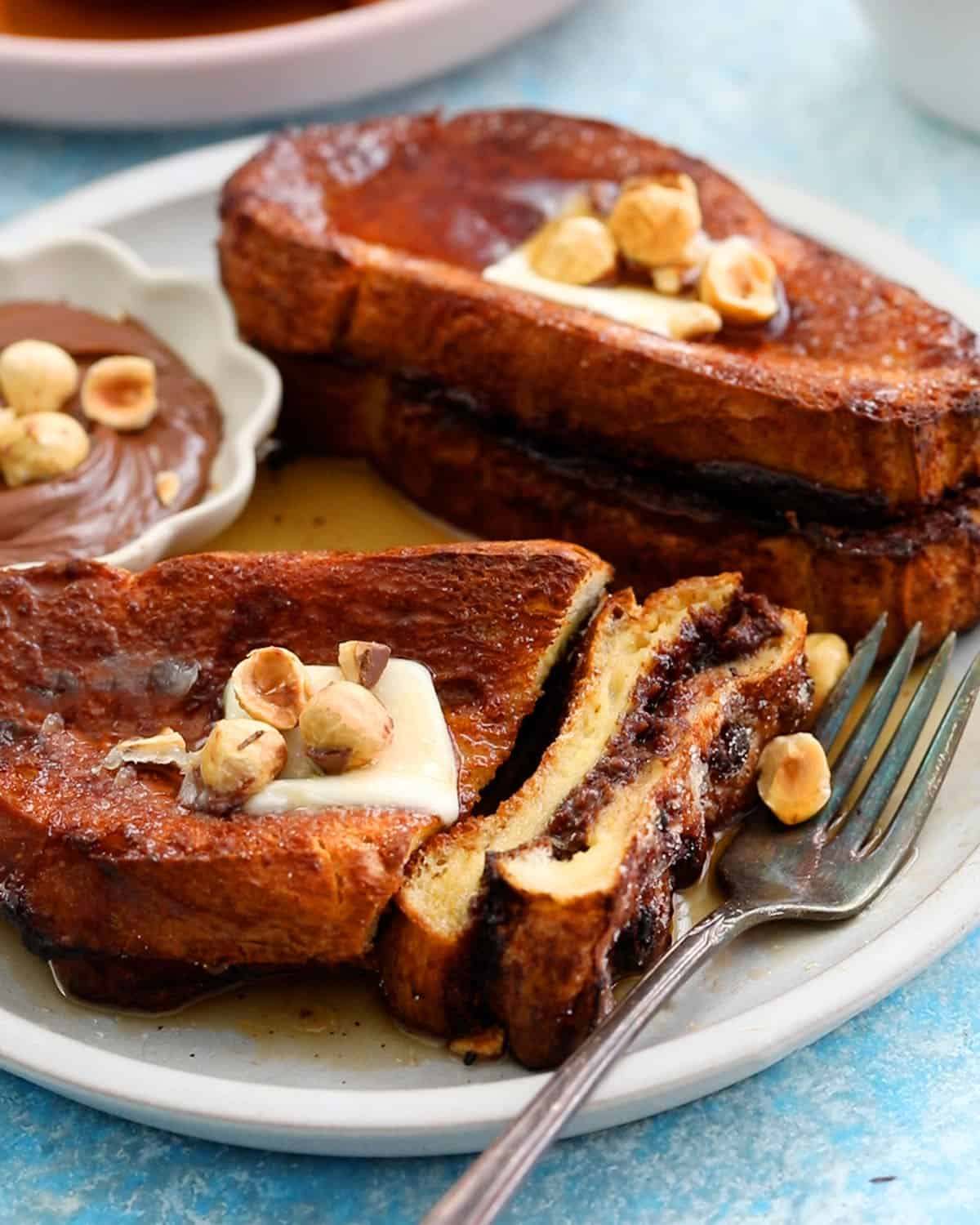 two brown French toasts topped with butter and hazelnuts in a white plate.