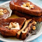 two brown French toasts topped with butter and hazelnuts in a white plate.