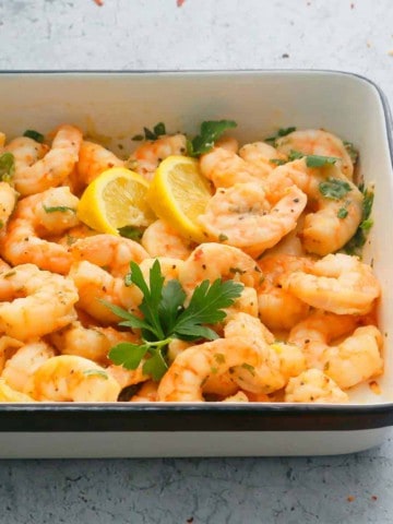 air fryer garlic shrimp placed in a white platter garnished with parsley and lemon wedges