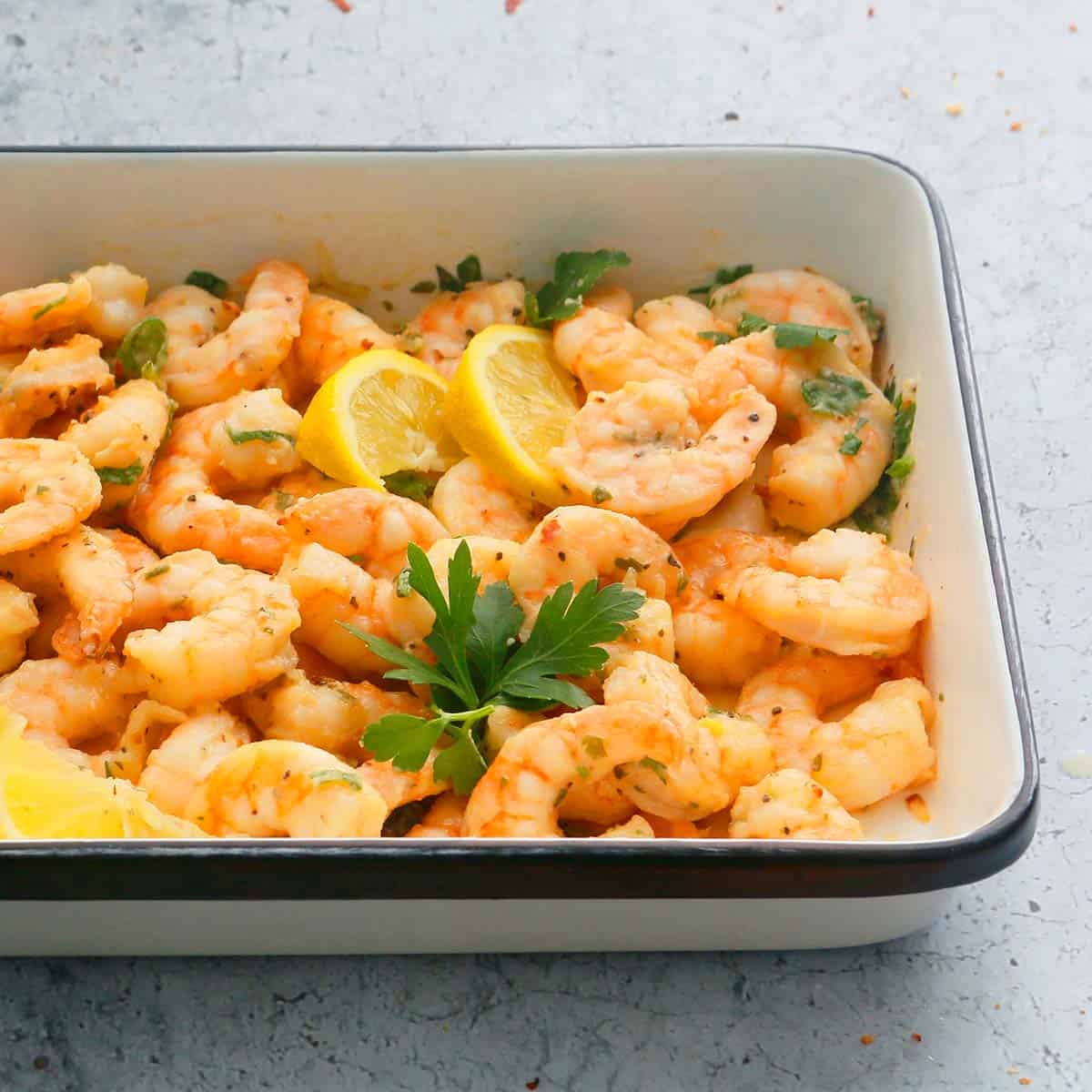 air fryer garlic shrimp placed in a white platter garnished with parsley and lemon wedges