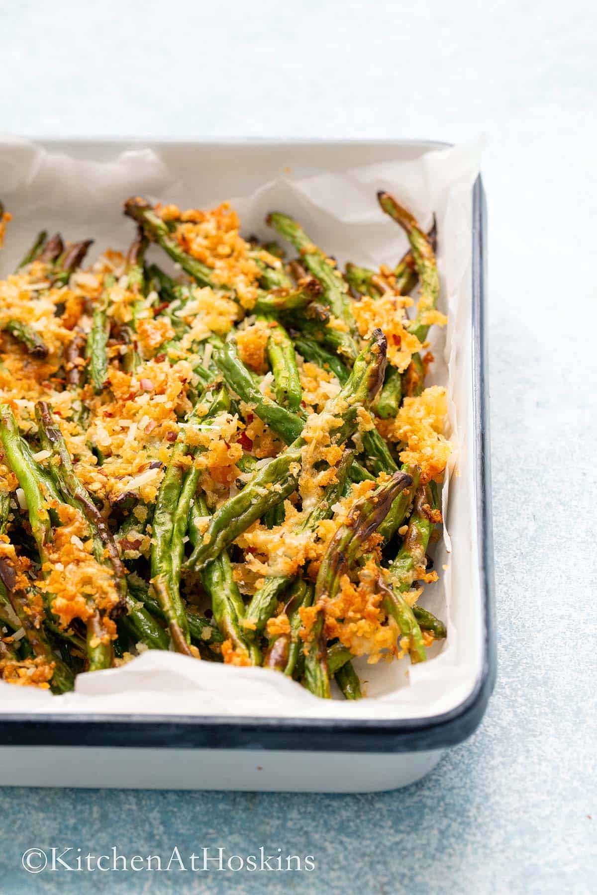 crispy air fried green beans with parmesan crust in a white tray.