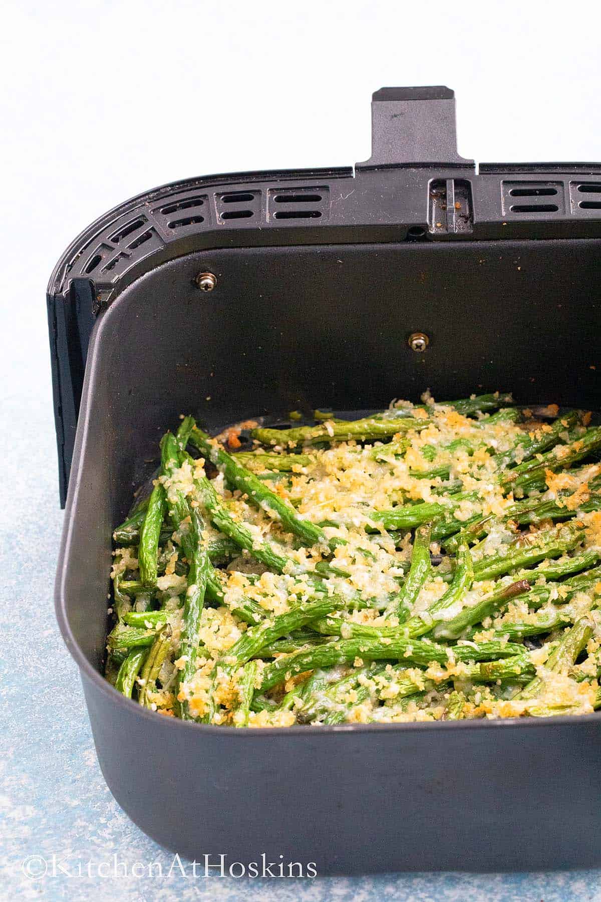 air fryer basket with roasted green beans topped with parmesan cheese.